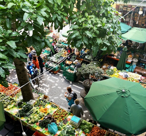 people standing near patio umbrella surrounded with fruits and vegetable stalls