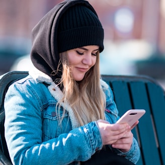woman holding smartphone while sitting on bench