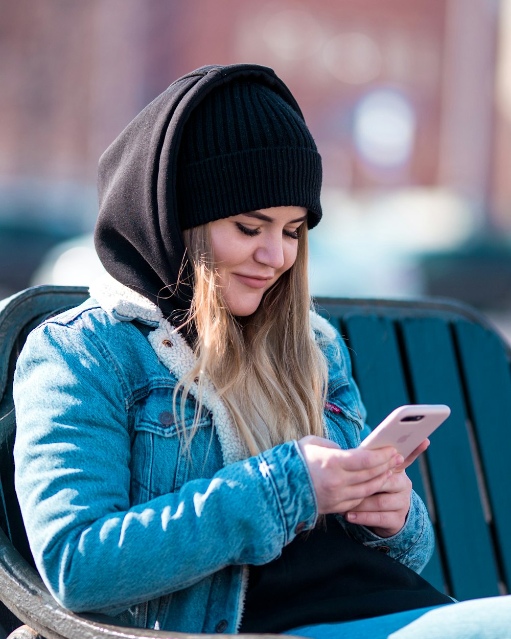 woman holding smartphone while sitting on bench