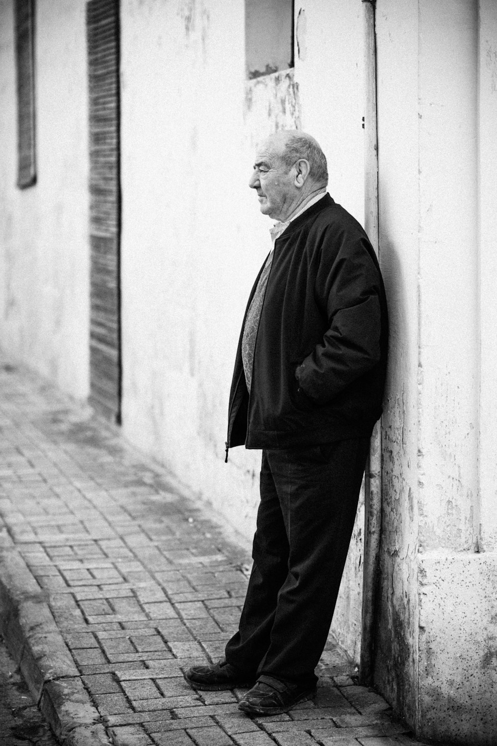 grayscale photography of man leaning against wall