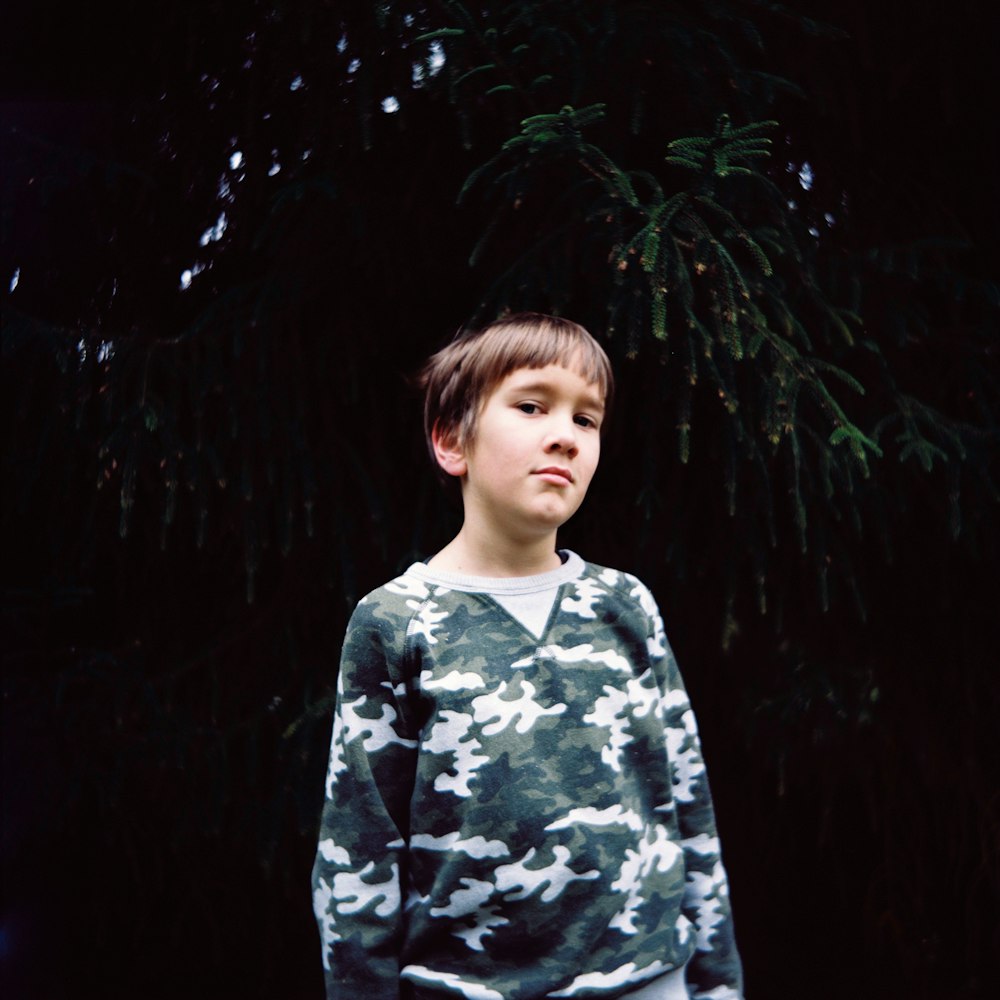 standing boy wearing brown and gray camouflage sweater