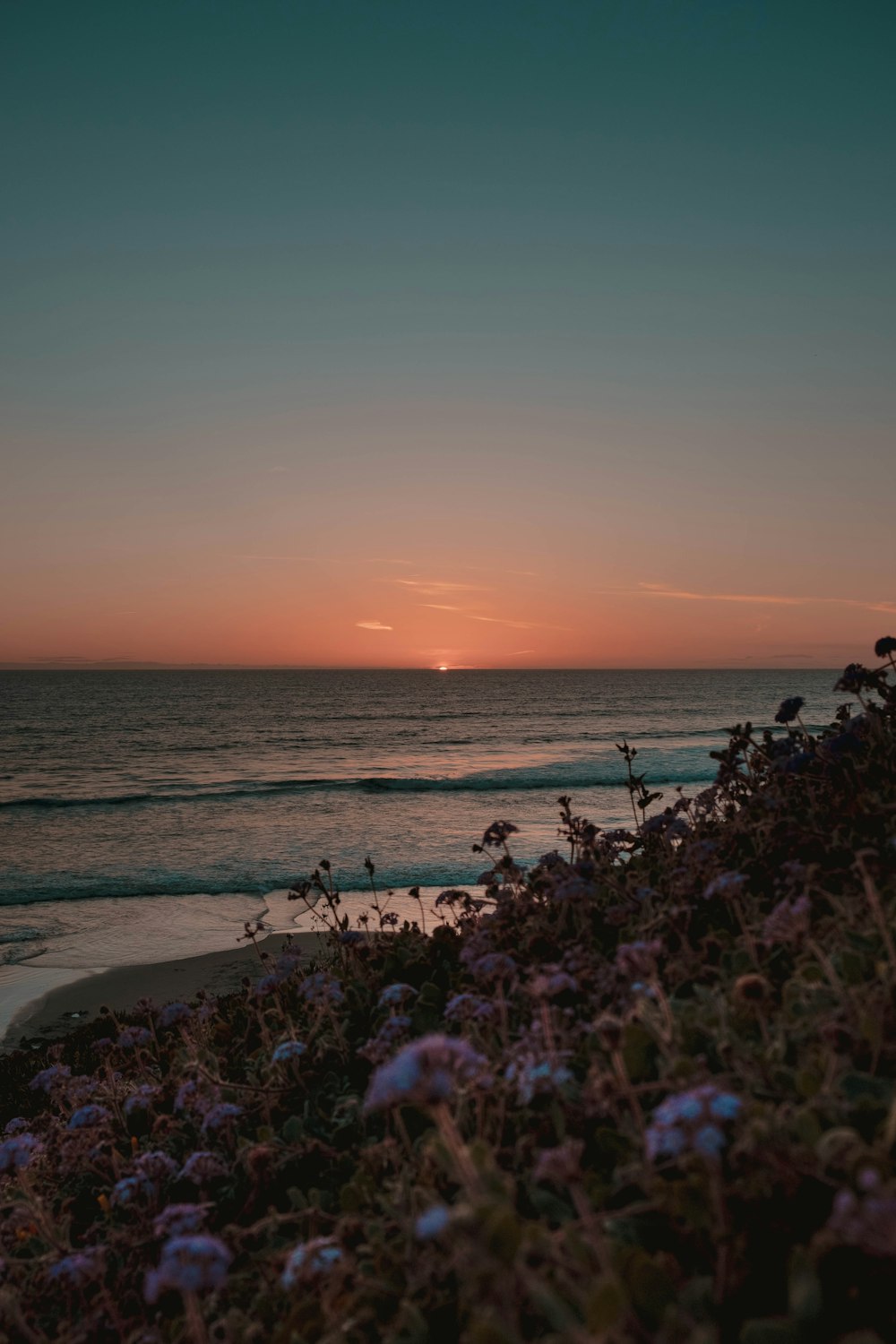 the sun is setting over the ocean on the beach