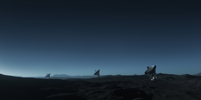 Three large satellite dishes stand on a dark, barren landscape under a deep blue sky. The scene appears to be desolate, with rocky terrain extending into the distance. The satellite dishes are evenly spaced and pointed towards the sky, suggesting a purpose of capturing signals from space. The horizon line is barely visible, shrouded in the twilight or early dawn light, creating a serene and somewhat mysterious atmosphere.