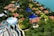 An aerial view of a resort with several red-roofed villas nestled among lush greenery. A large, winding swimming pool runs through the complex. There is also a water park section featuring multiple pools and slides. The resort is located near a body of water, possibly a lake or sea.