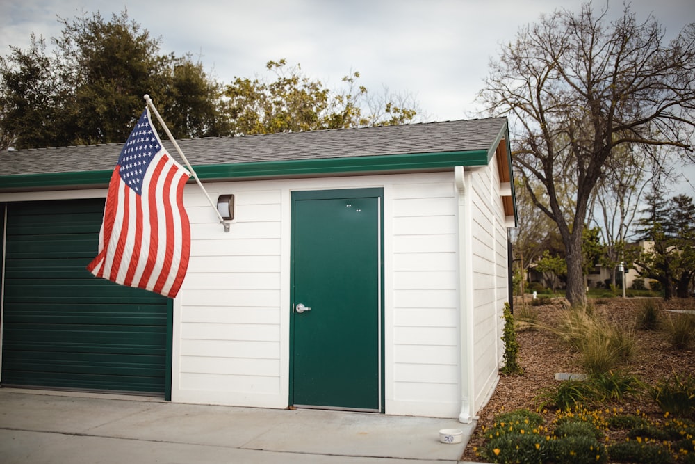 American flag outside white and green wooden house with closed door