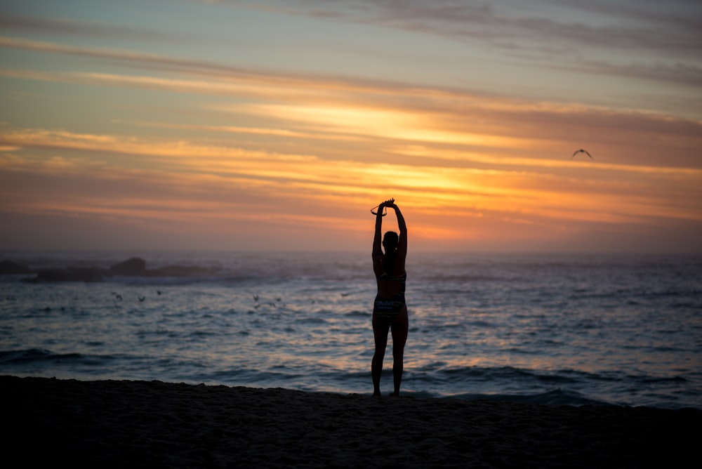 silhouette of woman standing beside seashore during sunset