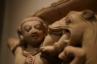 A close-up of an intricate stone sculpture featuring a human figure with detailed facial expressions and a horse's head. The sculpture showcases fine craftsmanship in the depiction of facial features and textures.