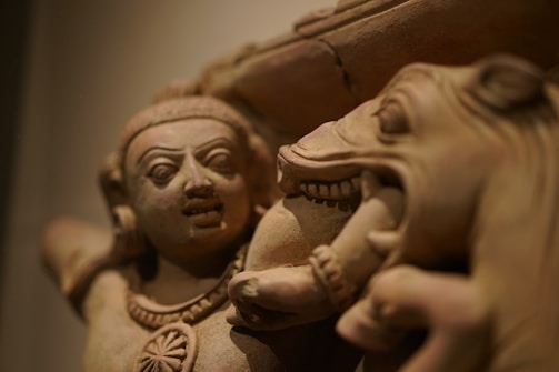 A close-up of an intricate stone sculpture featuring a human figure with detailed facial expressions and a horse's head. The sculpture showcases fine craftsmanship in the depiction of facial features and textures.