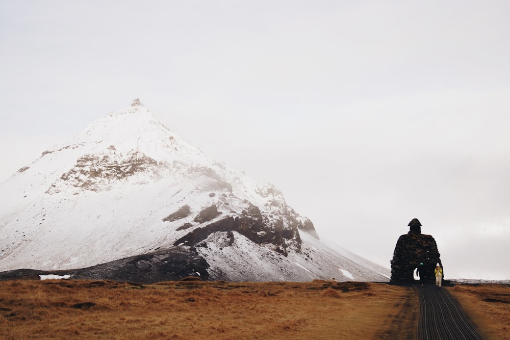 a man standing on a dirt road in front of a snow covered mountain