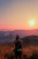 A joyful traveler standing on a mountain peak overlooking a vibrant sunset.