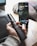 A person is holding a vaporesso vape mod in their hand. In the background, there is a smartphone placed on a wooden surface, displaying a lock screen. The setting appears to be indoors, possibly a home or office environment, with soft natural light illuminating the scene.