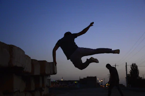 A dynamic screenshot of Jesús Run showing the character mid-parkour leap over urban rooftops at sunset.