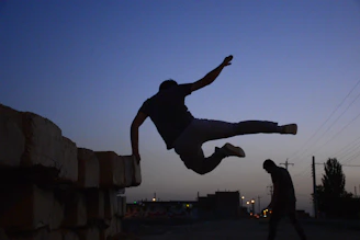 A dynamic screenshot of Jesús Run showing the character mid-parkour leap over urban rooftops at sunset.