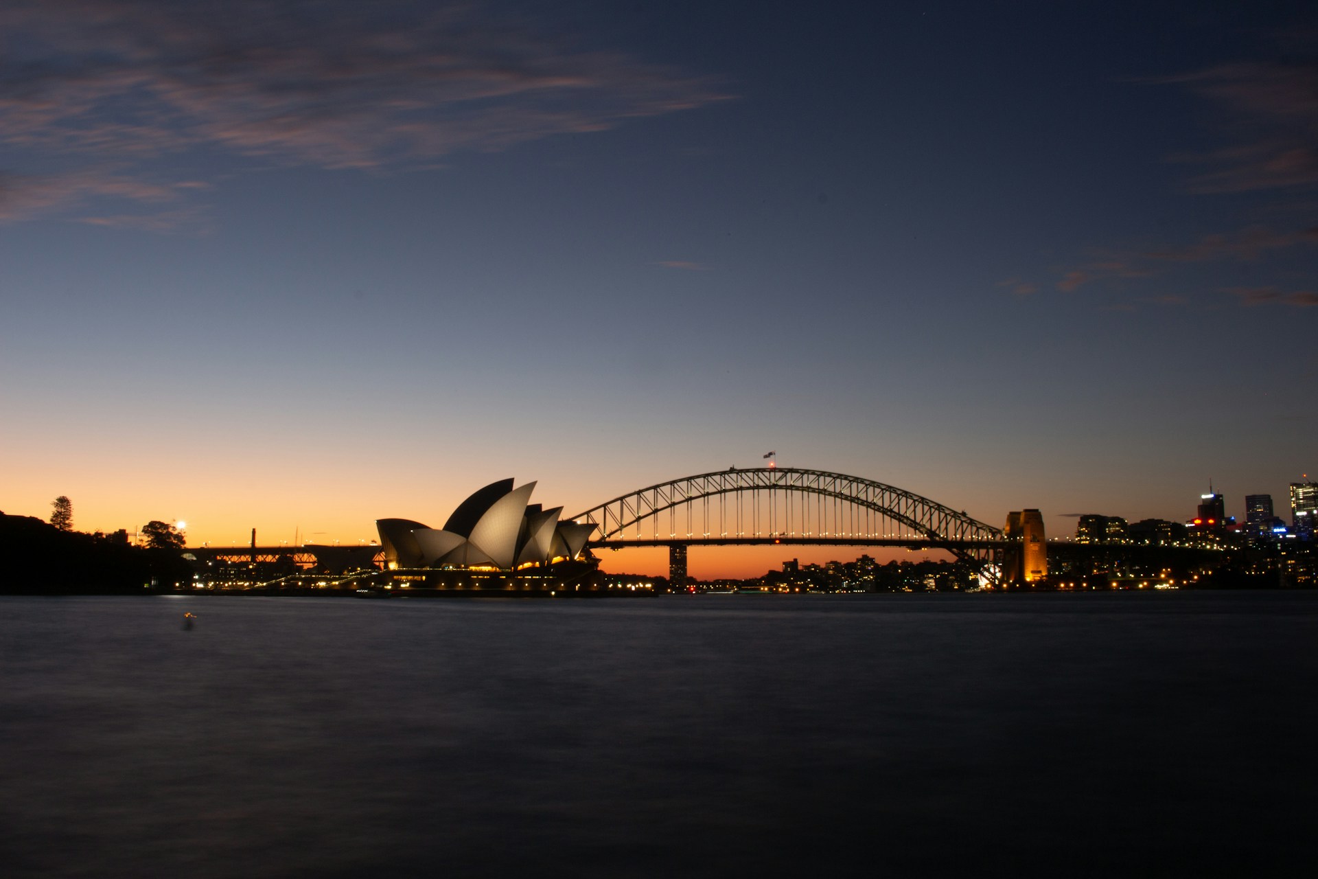 A serene sunrise over Sydney Harbour with the iconic Opera House and Harbour Bridge glowing warmly.