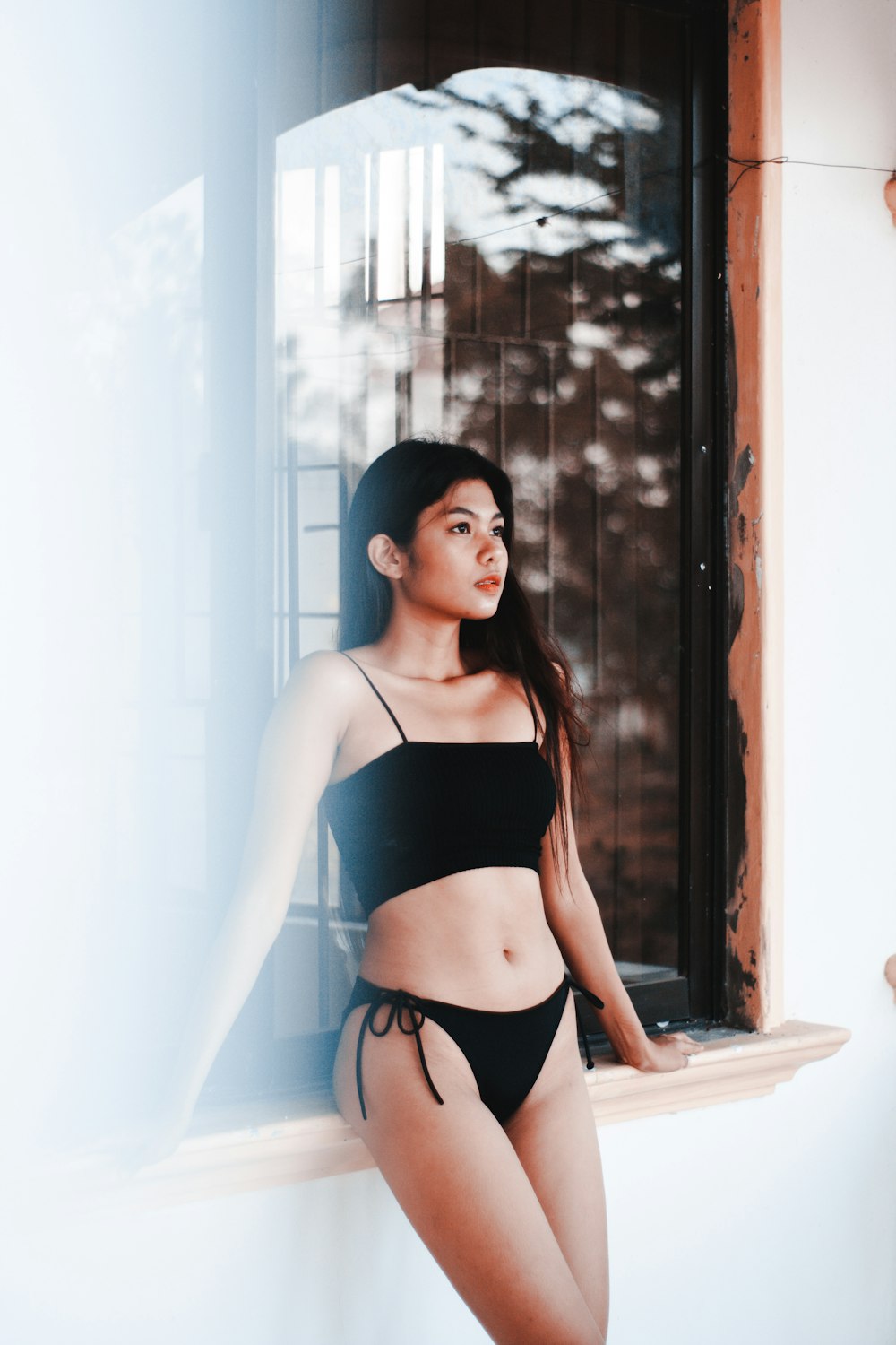 woman leaning on window wearing black bikini