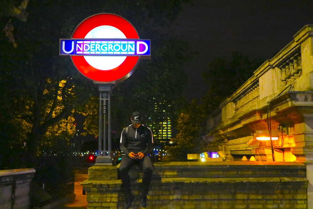 man sitting beside Underground LED signage during daytime
