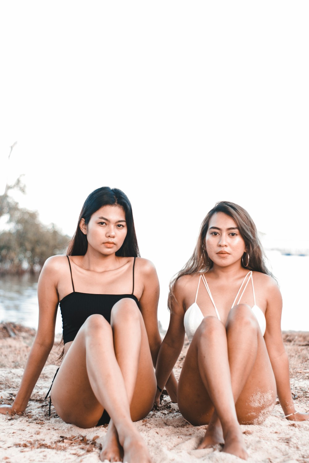two women wearing bikinis while sitting on shoreline