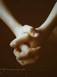Hands joined together in solidarity against a dark background with sky blue light.