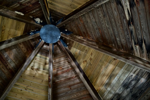 The interior view of a wooden ceiling with a geometric design, featuring a central circular hub. The ceiling is constructed using wooden panels that radiate outward in a symmetrical pattern.