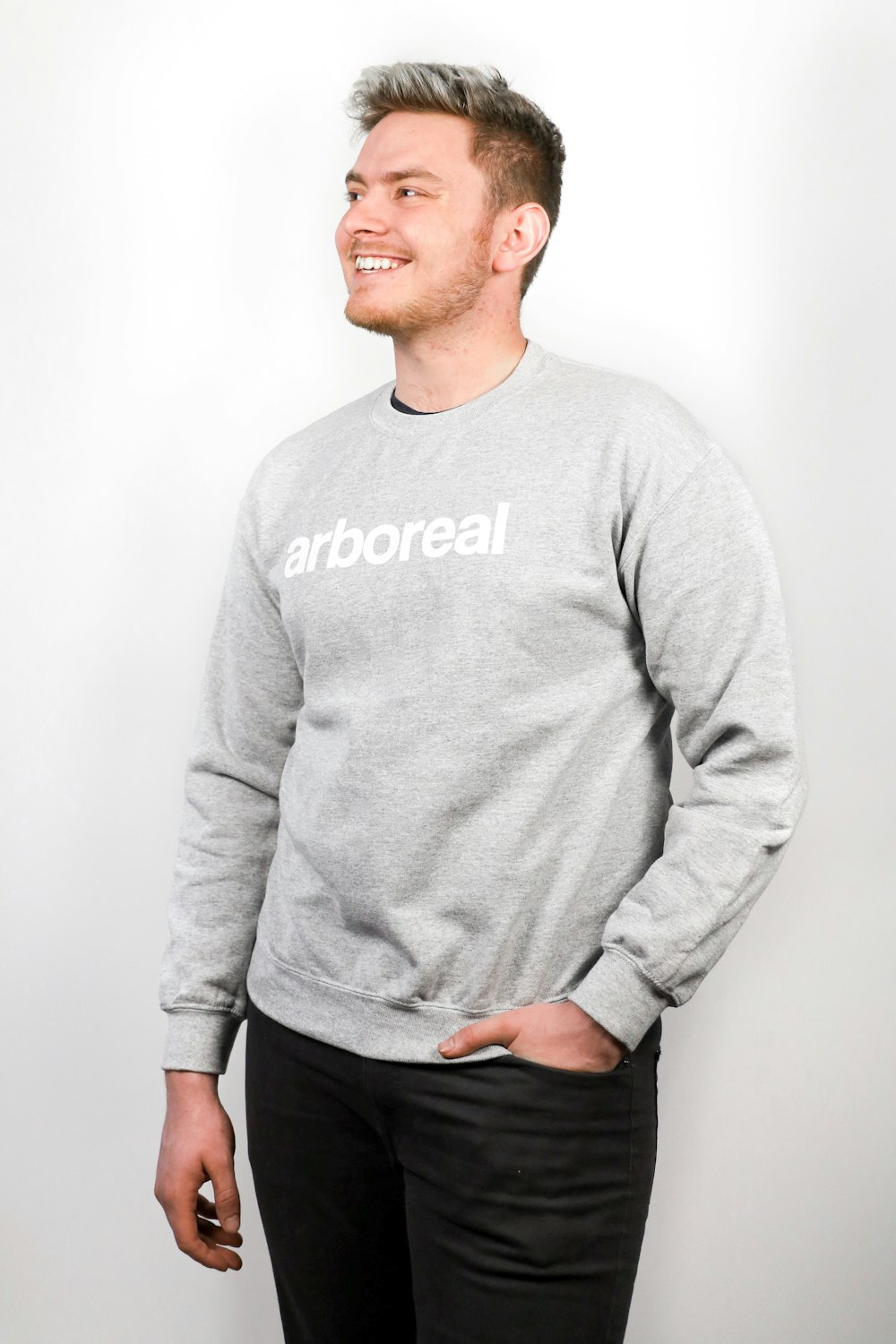 smiling man swearing gray sweater and black bottoms standing and looking his right side