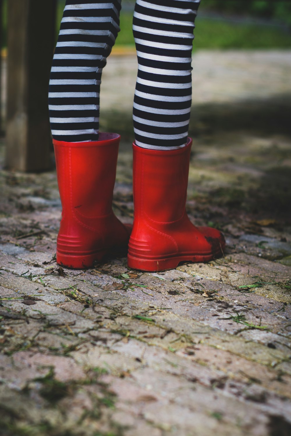 person wearing black and white striped socks and red rain boots standing on concrete pavement