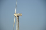 A tall wind turbine with three blades is set against a clear blue sky. The equipment is labeled with 'Solon 1250' on the nacelle, which is mounted on a lattice-style tower.