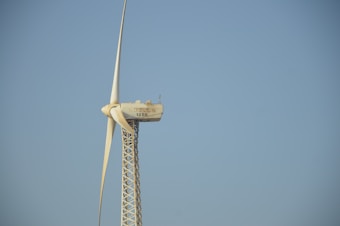 A tall wind turbine with three blades is set against a clear blue sky. The equipment is labeled with 'Solon 1250' on the nacelle, which is mounted on a lattice-style tower.