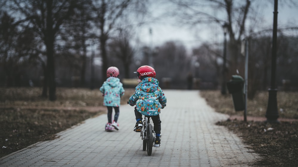 child riding with bike and another child walking on concrete pavement near trees