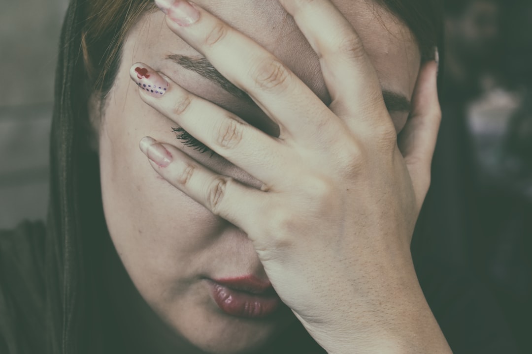 Person resting a hand over their face, overwhelmed by the emotional and physical symptoms of betrayal trauma