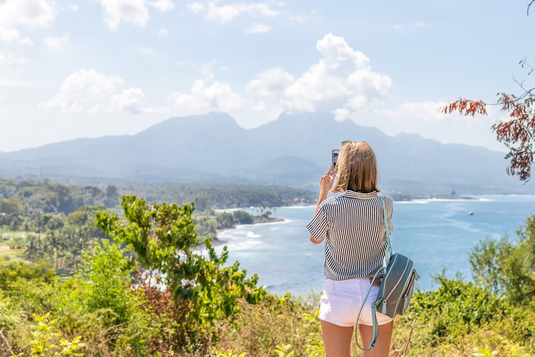 a woman taking a picture of the ocean with her cell phone,