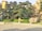 A meticulously landscaped garden featuring carefully trimmed trees with lush, rounded canopies. Large ornamental rocks are strategically placed throughout the garden, which is enclosed by a low stone fence. The setting is sunlit, casting soft shadows on the neatly paved ground.