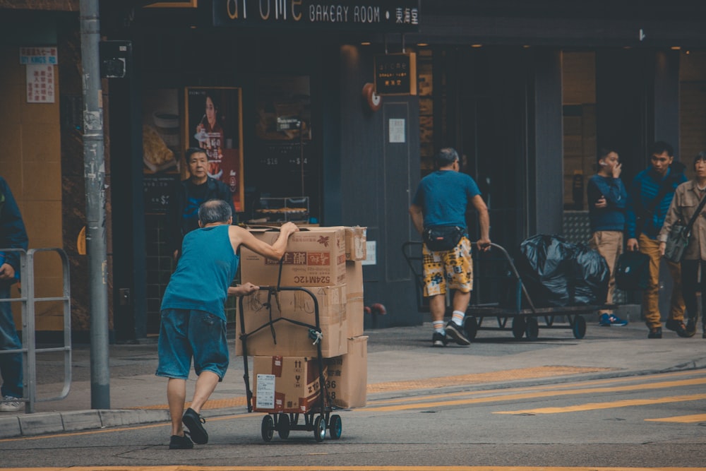 man wearing blue tank top pushing the hand truck with cardboard box