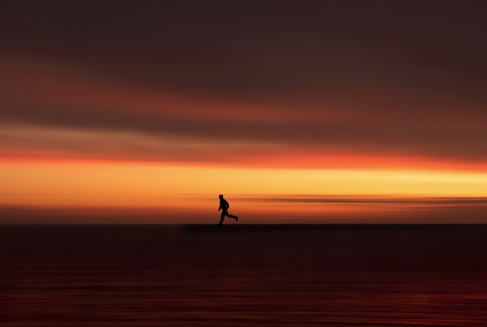 silhouette of person walking on the field during sunset