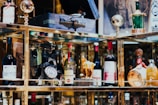 A collection of vintage and decorative bottles, an antique rotary phone, and other eclectic items are displayed on shelves with reflective surfaces.