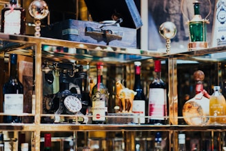 A collection of vintage and decorative bottles, an antique rotary phone, and other eclectic items are displayed on shelves with reflective surfaces.