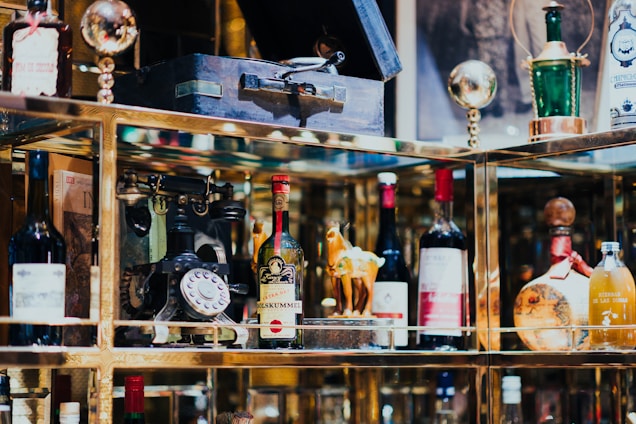 A collection of vintage and decorative bottles, an antique rotary phone, and other eclectic items are displayed on shelves with reflective surfaces.