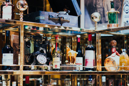 A collection of vintage and decorative bottles, an antique rotary phone, and other eclectic items are displayed on shelves with reflective surfaces.