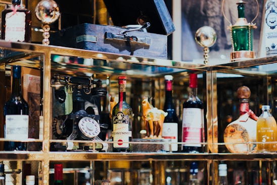A collection of vintage and decorative bottles, an antique rotary phone, and other eclectic items are displayed on shelves with reflective surfaces.