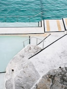A concrete slab pool with a whirlpool section surrounded by lounge chairs, hydromassage on, and a glass-fronted living room in the background, no people.