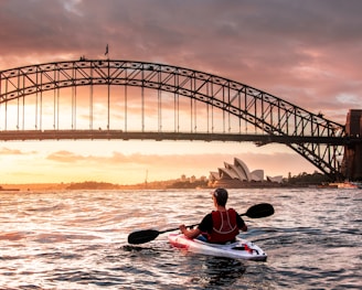 person riding kayak towards metal bridge