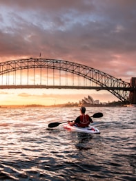 person riding kayak towards metal bridge