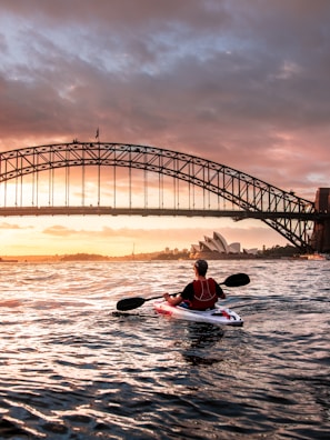 person riding kayak towards metal bridge