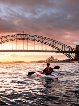 person riding kayak towards metal bridge