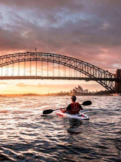 person riding kayak towards metal bridge