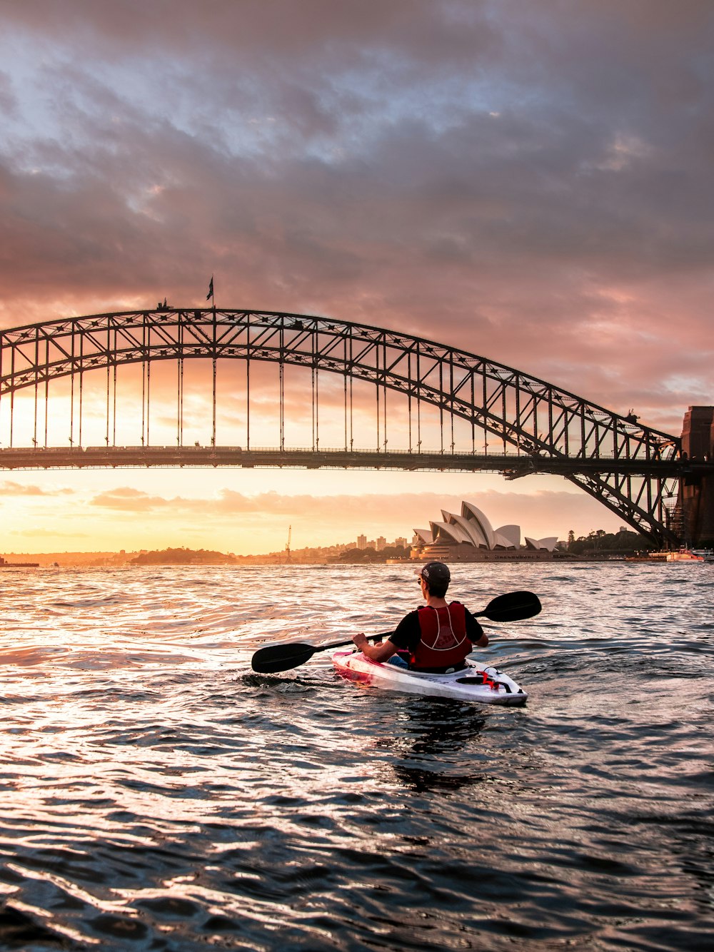 Persona montando kayak hacia el puente de metal
