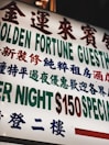 A brightly lit sign with text in both Chinese and English, featuring large, bold characters advertising a guesthouse. The sign prominently displays pricing information in red and green.