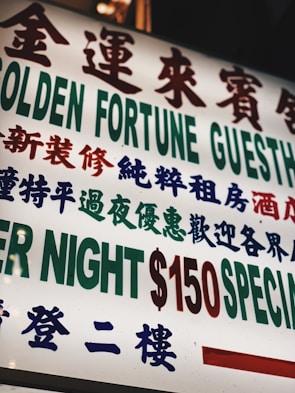 A brightly lit sign with text in both Chinese and English, featuring large, bold characters advertising a guesthouse. The sign prominently displays pricing information in red and green.