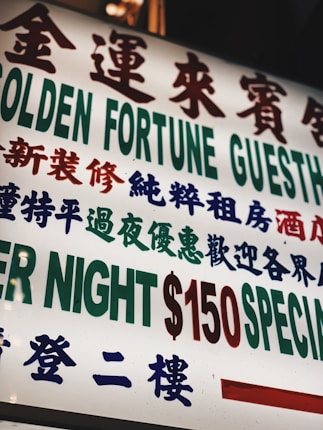 A brightly lit sign with text in both Chinese and English, featuring large, bold characters advertising a guesthouse. The sign prominently displays pricing information in red and green.