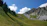 A serene mountain landscape with pilgrims trekking towards a distant peak under a clear blue sky.