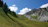 A serene mountain landscape with pilgrims trekking towards a distant peak under a clear blue sky.